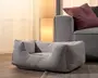 Blød lysegrå rektangulær kæledyrsseng med polstrede sider, lav åbning foran og en forsænket liggeflade, vist på et trægulv ved siden af en sofa.