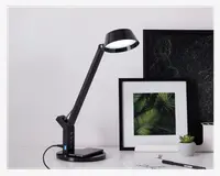 Elegant, moderne sort skrivebordslampe med justerbar arm og rundt lampehoved. Lampen har et touch-kontrolpanel i basen, som også indeholder USB-opladningsporte. Lampen er tændt og har en solid, vægtet base for stabilitet. Designet er minimalistisk og passer til moderne arbejdsområder.