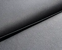 Nærbillede af et sort materiale med en fin, småkornet tekstur og mat finish. Overfladen ser smidig og fleksibel ud med en let glans, der fremhæver kornmønsteret. Billedet viser en foldet kant, hvilket indikerer materialets tykkelse og bøjelighed.