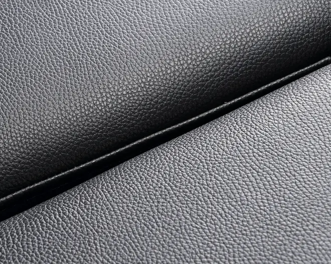 Nærbillede af et sort materiale med en fin, småkornet tekstur og mat finish. Overfladen ser smidig og fleksibel ud med en let glans, der fremhæver kornmønsteret. Billedet viser en foldet kant, hvilket indikerer materialets tykkelse og bøjelighed.