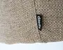 Nærbillede af et tekstureret, vævet stof i en naturlig beige farve. Materialet har et groft, kurvevævet mønster, hvilket giver det et rustikt og holdbart udseende. En lille sort stofmærke med hvid tekst, hvor der står 'daells', er syet ind i sømmen og angiver mærket. Syningerne er synlige, hvilket viser omhu i udførelsen.