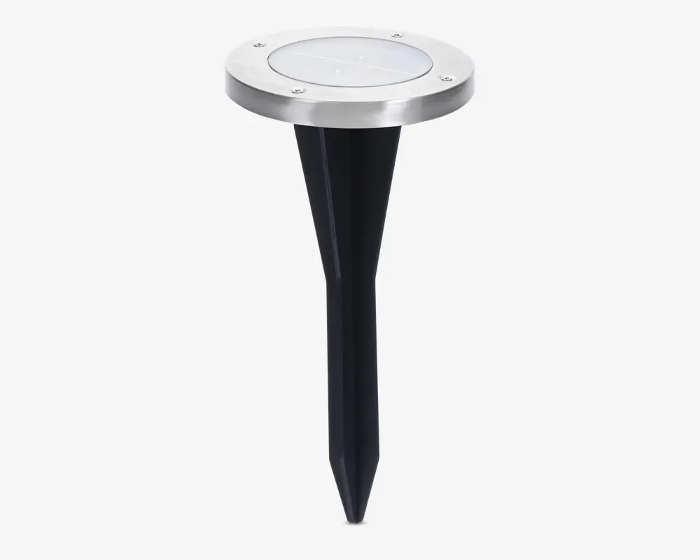 Rund udendørs jordlampe med top i rustfrit stål og klart linse, udstyret med sort spids jordspyd for nem montering i jorden. Toppen har fire synlige skruer, der fastgør linsen, og designet er stilrent og moderne.