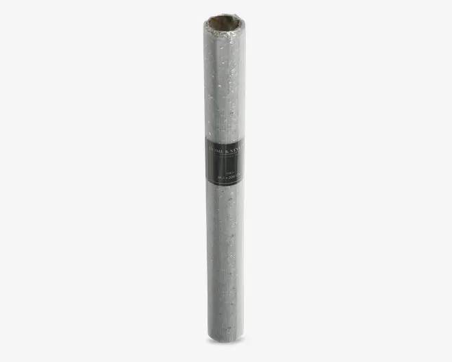 En rulle gavepapir med sølvfarvet, metallisk finish og et diskret mønster af små, spredte stjerner. Papiret har en blank overflade, hvilket giver det et festligt og elegant udseende. Rullen er samlet med en sort etiket omkring midten, hvor produktinformation vises.