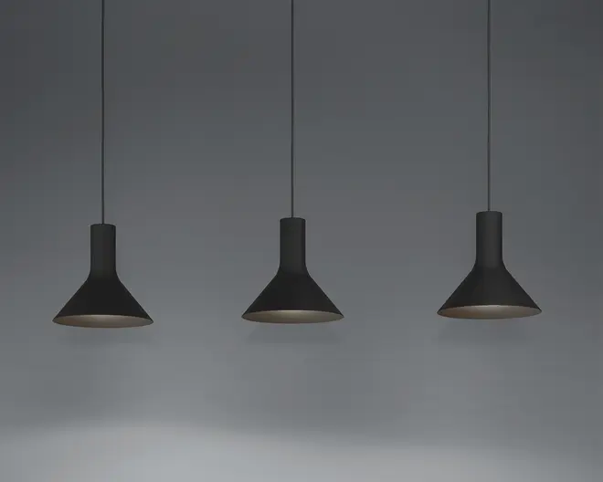 Tre pendellamper med mat sort finish, hver med en bred, konisk skærm og en slank cylindrisk hals. Lamperne hænger fra tynde sorte ledninger og har et minimalistisk og moderne udtryk. Indersiden af skærmene ser ud til at være lysere, hvilket forbedrer lysrefleksionen.