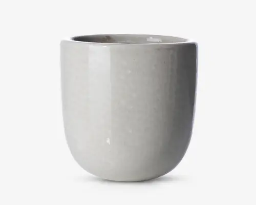 En glat, rund keramisk beholder med en blank lysegrå overflade. Overfladen er jævn og uden dekoration, hvilket giver et minimalistisk og moderne udtryk. Kanten er let tyk, og formen er cylindrisk med en blødt buet bund.