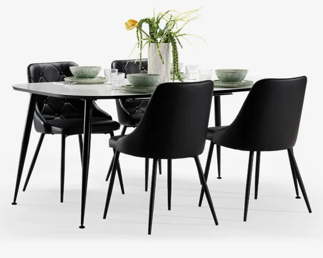 Moderne spisebordssæt med et rektangulært bord, der har en elegant hvid bordplade og slanke sorte metalben. Sættet inkluderer seks sorte stole, hvoraf fire har glatte, buede rygge og to har ryglæn og sæde med knapdetaljer, alle med slanke sorte ben. Bordet er dækket med grønne keramiske skåle og tallerkener, klart glas og en hvid vase med blandet grønt og en gul blomst, hvilket skaber et stilfuldt og indbydende udtryk.