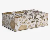 Rektangulær æske med hængslet låg, dekoreret med et hvidt baggrund og et detaljeret blomstermønster i guld, grøn og diskrete lavendelfarver. Blomsterne og bladene er fint udført, og nogle elementer har en metallisk guldfinish, der giver et elegant og luksuriøst udtryk. Æsken har skarpe kanter og en glat, blank overflade.