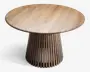 Rundt bord i træ med en glat bordplade, der viser naturlig træstruktur. Bordet har en markant piedestal-fod bestående af lodrette trælameller med mellemrum imellem, hvilket giver et let og moderne udtryk. Foden udvider sig let mod gulvet for et stilfuldt design.