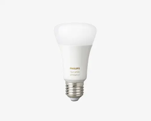 En moderne LED-pære med mat hvid top og standard skruefatning. Pæren har et glat, afrundet design og teksten 'PHILIPS Hue white ambiance' er trykt på siden i guld og grå. Overfladen er glat, og pæren er designet til intelligente belysningssystemer med mulighed for justerbare hvide lysnuancer.
