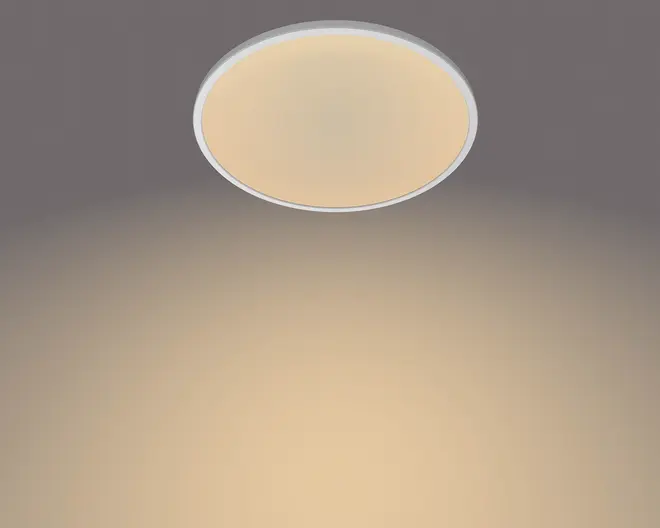 Rund loftlampe til planmontering med smal hvid kant og frostet beige diffuser, vist med et varmt og blødt lys på loftet.