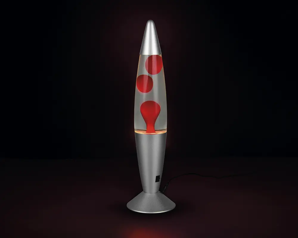 En høj, raketformet lampe med en metallisk sølvfarvet fod og top. Den gennemsigtige midtersektion indeholder røde voksbobler, der flyder i en klar væske og skaber en dynamisk, bevægelig effekt, når lampen er tændt. Lampen får strøm via en ledning, der er synlig ved foden.