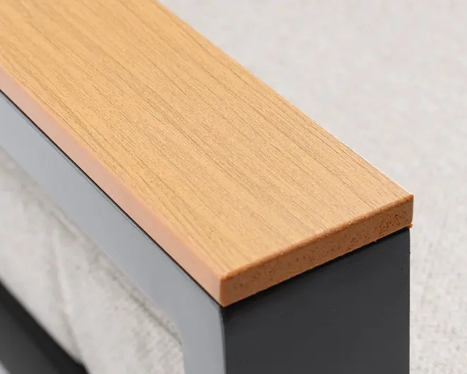 Nærbillede af et rektangulært armlæn med en lys træstruktur på toppen og glatte, lige kanter. Armlænet er understøttet af en solid, mørk metalramme, og træoverfladen ser ud til at være lamineret eller belagt for øget holdbarhed.