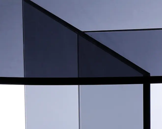 Nærbillede af en geometrisk struktur lavet af tonede glasplader med sorte metalrammer. Glasset har en mørk, røgfarvet nuance, og pladerne er arrangeret i vinklede, overlappende former, hvilket giver et moderne og minimalistisk udtryk. Overfladerne reflekterer lyset diskret og fremhæver de rene linjer og skarpe kanter i designet.