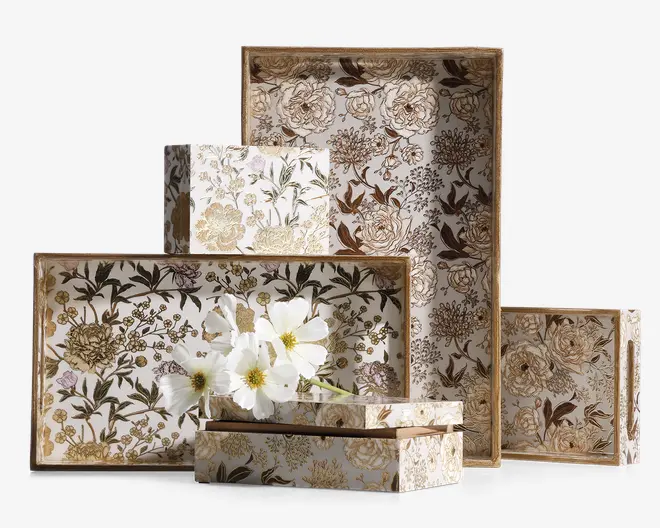 Sæt af dekorative rektangulære og firkantede æsker i forskellige størrelser med et elegant blomstermønster i nuancer af guld, brun og creme. Æskerne har et vintage-inspireret design med detaljerede botaniske illustrationer, og nogle har guldfarvede kanter. Overfladerne er blanke, hvilket giver et raffineret og luksuriøst udtryk. En af æskerne er åben og indeholder hvide kunstige blomster, hvilket fremhæver æskernes anvendelse til både opbevaring og dekoration.