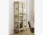 Høj vitrineskab med lys træramme og glaslåger, udstyret med tre glashylder til opbevaring. Skabet står på fire skråtstillede ben, hvilket giver et moderne, retro-inspireret udtryk. Indretningen er rummelig og gør det nemt at se de placerede genstande, såsom bøger, skåle og dekorative objekter.