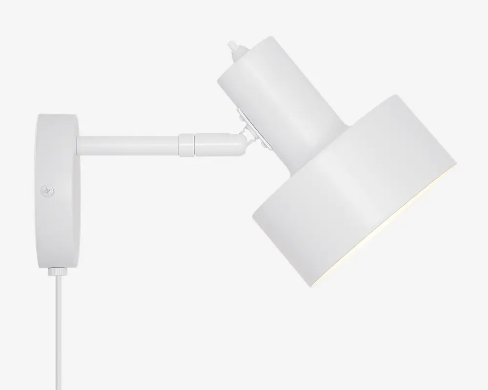 Moderne vægmonteret lampe med mat hvid finish, cylindrisk justerbar arm og bred, vinklet lampeskærm. Lampen har en synlig ledning og et enkelt, minimalistisk design, der passer til moderne indretning.