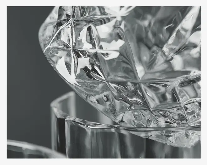 Nærbillede af et klart glasobjekt med et detaljeret, facetslebet mønster med stjerne- og diamantformer. Glasset har en meget blank, reflekterende overflade og tykke vægge, hvilket giver et indtryk af holdbarhed og høj kvalitet.