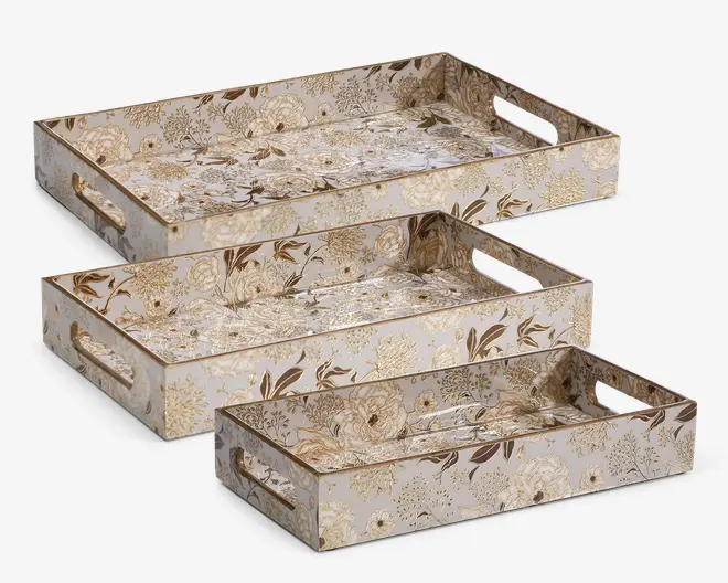 Sæt med tre rektangulære bakker i forskellige størrelser, hver med et beige og gyldent blomsterdesign med fine detaljer. Bakkerne har forhøjede kanter og udskårne håndtag i begge ender for nem transport. Blomsterdesignet dækker både indersiden og ydersiden, hvilket giver et sammenhængende og elegant udseende. Bakkerne kan stables inden i hinanden for praktisk opbevaring.