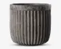 En rund, grå potte med lodret riflede sider. Overfladen har et betonlignende udseende, hvilket giver et moderne og industrielt præg. Den øverste kant er glat og en smule bredere end selve kroppen, hvilket skaber en diskret kant.
