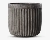 En rund, grå potte med lodret riflede sider. Overfladen har et betonlignende udseende, hvilket giver et moderne og industrielt præg. Den øverste kant er glat og en smule bredere end selve kroppen, hvilket skaber en diskret kant.