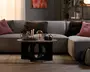 Rund bordplade i naturligt trælook med en skulpturel sort geometrisk base med store ovale udskæringer og en lav, moderne profil.