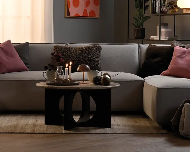 Rund bordplade i naturligt trælook med en skulpturel sort geometrisk base med store ovale udskæringer og en lav, moderne profil.