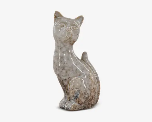 Keramikfigur formet som en siddende kat med en blank, plettet beige og brun overflade. Overfladen er glat med diskrete farvevariationer, og kattens ansigtstræk og kropskonturer er let markeret. Figuren har en let forlænget hals og oprejste ører, hvilket giver et elegant udtryk.