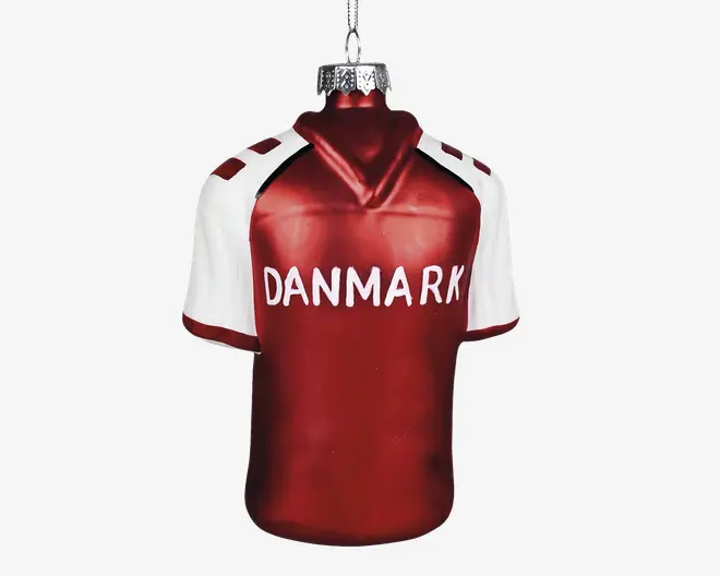 Et juleornament formet som en sportstrøje med rød krop og hvide ærmer samt skulderdetaljer. Ordet 'DANMARK' står skrevet med store hvide bogstaver på brystet. Ornamentet har en sølvfarvet top og ophæng til at hænge på juletræet.