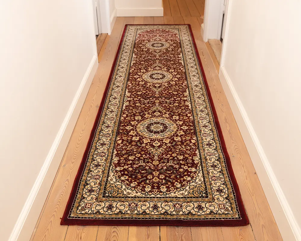 Lang, rektangulær løber med en dyb bordeaux baggrund og detaljerede blomstermønstre i creme, guld og marineblå. Har tre store medaljonmotiver jævnt fordelt langs midten. Kanten er dekoreret med udsmykkede snørklede og blomsterdesigns i creme og guld nuancer. Tæppet har lav luv og ser tæt vævet ud, hvilket gør det velegnet til områder med meget trafik som gange.