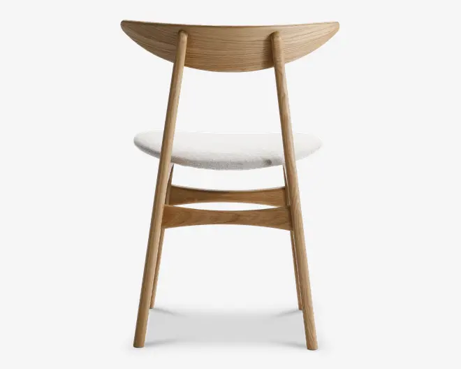 Stol med stel i lyst naturtræ, buet halvmåneformet ryglæn og skråtstillede bagben. Sædet er polstret med et lyst stof, som giver en blød kontrast til træet. Designet er minimalistisk og moderne med rene linjer og synlig træstruktur.