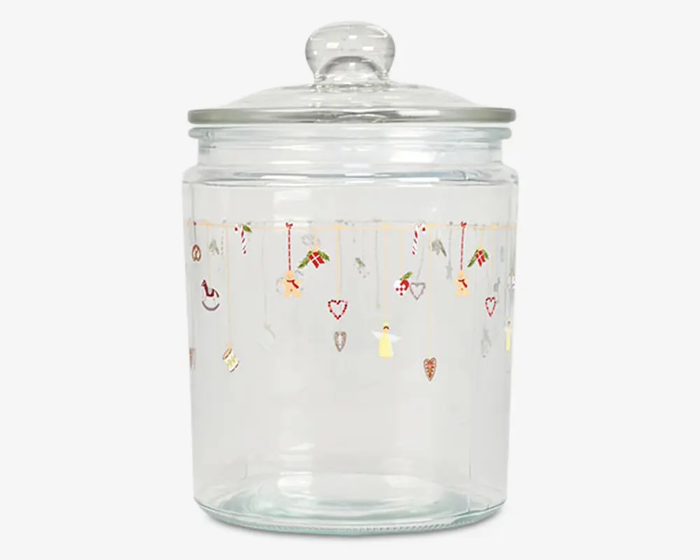 Klar glasbeholder med rundt låg og knop som håndtag. Beholderen har et festligt design øverst med små illustrationer af julemotiver som slikstokke, hjerter, gaver, engle og stjerner, der hænger ned fra gyldne linjer. Glasset er cylindrisk og har en glat, gennemsigtig overflade.