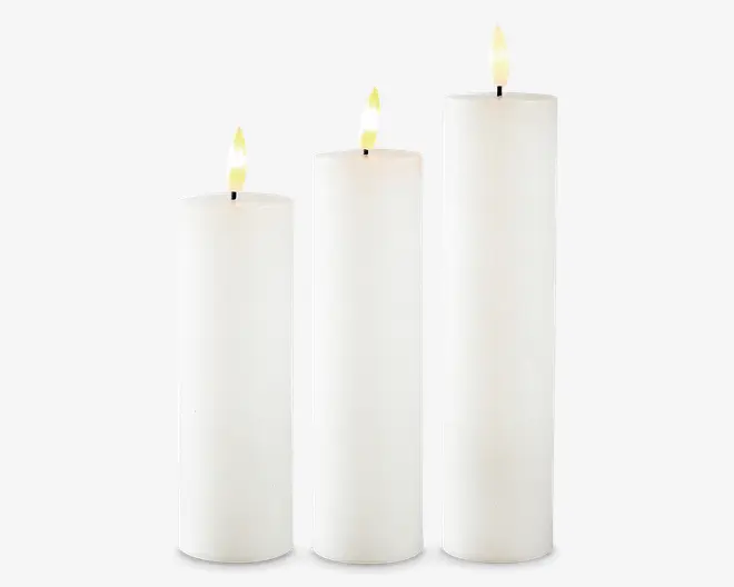 Sæt med tre cylindriske stearinlys i forskellige højder, alle med en glat, hvid voksfinish. Lysene har flade toppe og realistiske, let gullige kunstige flammer, hvilket antyder, at de muligvis er batteridrevne LED-lys. Det minimalistiske design gør dem velegnede til mange forskellige dekorative formål.