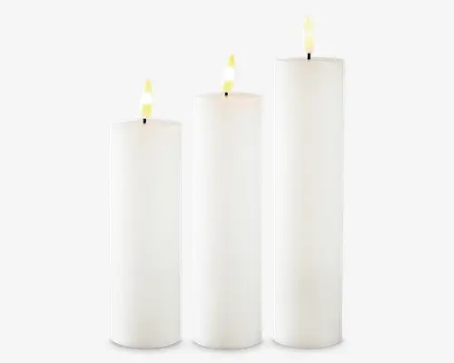 Sæt med tre cylindriske stearinlys i forskellige højder, alle med en glat, hvid voksfinish. Lysene har flade toppe og realistiske, let gullige kunstige flammer, hvilket antyder, at de muligvis er batteridrevne LED-lys. Det minimalistiske design gør dem velegnede til mange forskellige dekorative formål.