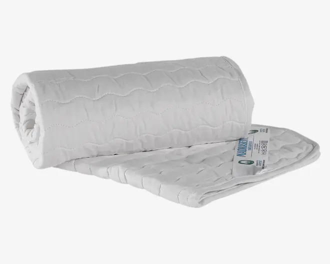 Hvid, quiltet madrasbeskytter med diskret bølget syning. Stoffet ser blødt ud og er let polstret for ekstra komfort. Kanterne er pænt afsluttede med en syet kant, og et produktmærkat med vaskeanvisninger og certificeringer ses i det ene hjørne. Beskytteren er delvist rullet sammen, hvilket viser dens fleksibilitet og tykkelse.