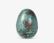 Æggeformet beholder med en tekstureret, irret kobberoverflade. Overfladen har en blanding af turkisgrønne og brunlige rustfarver, hvilket giver et antikt og vejrbidt udseende. Beholderen er delt vandret på midten, hvilket indikerer, at den kan åbnes for opbevaring af genstande indeni.