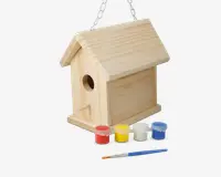 Umalet fuglehus af træ med sadeltag, rundt indgangshul og lille siddepind under indgangen. Fuglehuset hænger i en metal kæde. Foran fuglehuset står fire små malerbøtter i rød, gul, hvid og blå samt en tynd pensel, hvilket viser, at fuglehuset kan dekoreres.
