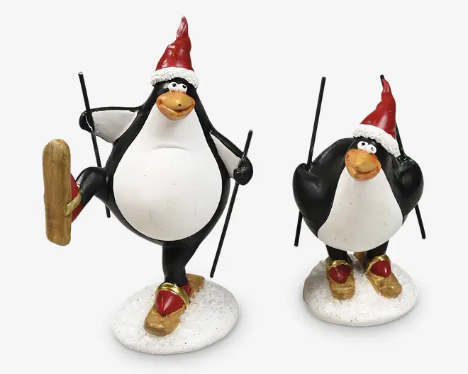 Sæt med to humoristiske pingvinfigurer iført røde nissehuer med hvid kant. Hver pingvin er udformet som om de står på ski, holder sorte skistave og står på hvide, sne-lignende baser. Pingvinerne har orange næb, udtryksfulde øjne og bærer røde sko fastgjort til træsko. Den ene pingvin løfter den ene ski i en legende positur, mens den anden står med begge ski på jorden.