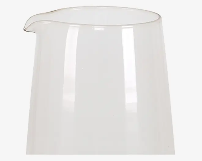 En klar, cylindrisk glaskande med bred åbning og en lille hældetud. Glasset har en glat, blank overflade og et enkelt, moderne design uden hank eller dekorative detaljer.