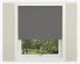 Et vindue med en mørkegrå rullegardin, der er delvist rullet ned og dækker den øverste halvdel af vinduet. Gardinet har et glat, ensfarvet stof uden synlige mønstre eller teksturer. Vinduesrammen er hvid, og væggen omkring er lysebeige. Den nederste del af vinduet giver udsyn til grønne træer og græs udenfor.