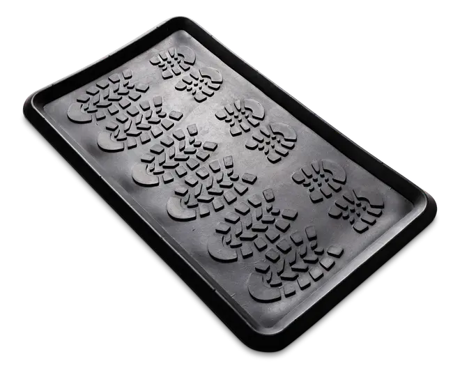 Rektangulær sort bakke af gummi med forhøjede kanter og en mønstret overflade med flere aftryk af støvlesåler. Bakken er designet til at opsamle snavs, vand eller skidt, og de hævede mønstre hjælper med at holde genstande over eventuel opsamlet fugt.