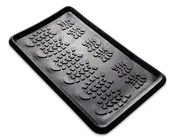 Rektangulær sort bakke af gummi med forhøjede kanter og en mønstret overflade med flere aftryk af støvlesåler. Bakken er designet til at opsamle snavs, vand eller skidt, og de hævede mønstre hjælper med at holde genstande over eventuel opsamlet fugt.