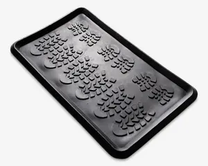 Rektangulær sort bakke af gummi med forhøjede kanter og en mønstret overflade med flere aftryk af støvlesåler. Bakken er designet til at opsamle snavs, vand eller skidt, og de hævede mønstre hjælper med at holde genstande over eventuel opsamlet fugt.