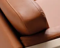 Nærbillede af et sofaarmlæn betrukket med glat, lysebrunt læder. Syningerne er syn sop langs kanterne, hvilket vidner om godt håndværk. Læderet har en let k impacting struktur, og polstringen ser tyk og støttende ud. Bunden af armlænet er lavet af lyst træ, hvilket giver et moderne udtryk.