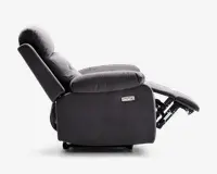 Sidebillede af en mørkegrå lænestol i fuldt tilbagelænet position. Stolen har bløde, polstrede armlæn og en polstret ryg for ekstra komfort. Fodstøtten er slået ud og understøttes af en synlig metalmekanisme. På siden er der et kontrolpanel med to knapper, hvilket indikerer elektrisk justering. Betrækket ser ud til at være af blødt stof.