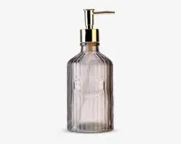 Gennemsigtig glasdispenserflaske med lodret rillet struktur, guldfarvet pumpe og ordet 'SOAP' præget på forsiden. Flasken har et vintage-inspireret design og en solid bund.