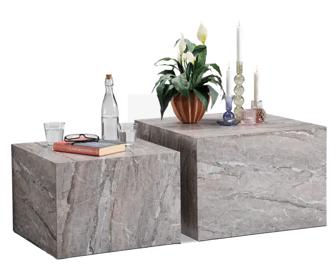 To kubeformede borde med et naturstenslook i grå og beige nuancer, med en glat, mat overflade og synlige åretegninger. Bordene er dekoreret med forskellige pyntegenstande, herunder en potteplante med hvide blomster, glaslysestager, en vandflaske, en bog med briller samt en samling af glaslysestager og vaser. Bordene har et moderne, minimalistisk design med rene linjer og et solidt, robust udtryk.