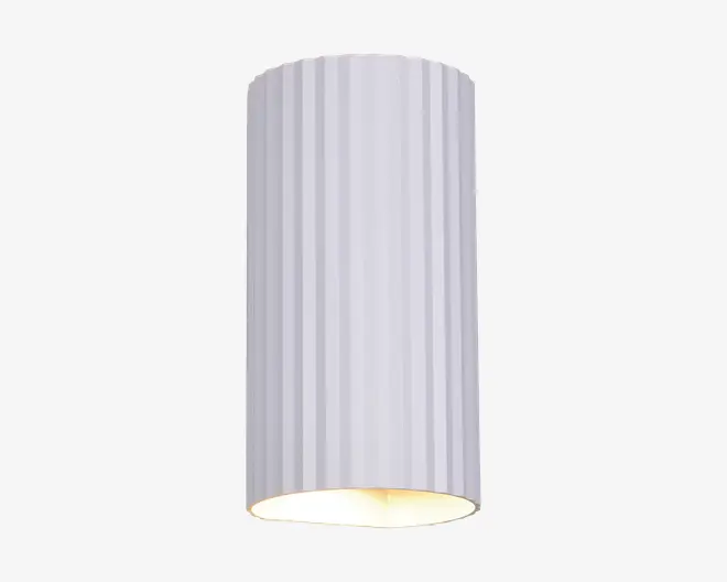 Høj, cylindrisk lampe med lodrette riller på overfladen og en mat hvid finish. Den åbne bund lader lyset skinne direkte nedad og giver et fokuseret lys. Designet er moderne og minimalistisk, velegnet til nutidige indretninger.