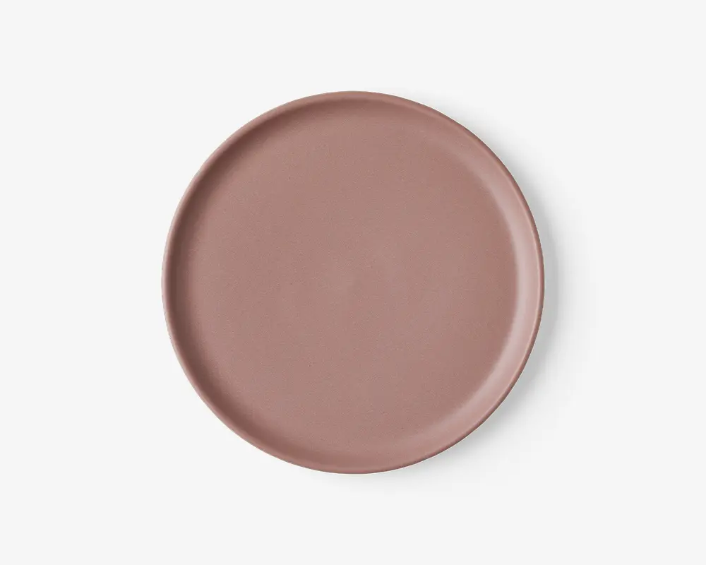 Rund tallerken med en glat, mat overflade i en afdæmpet rosa farve. Tallerkenen har en let forhøjet kant og et enkelt, minimalistisk design uden mønstre eller dekorationer.