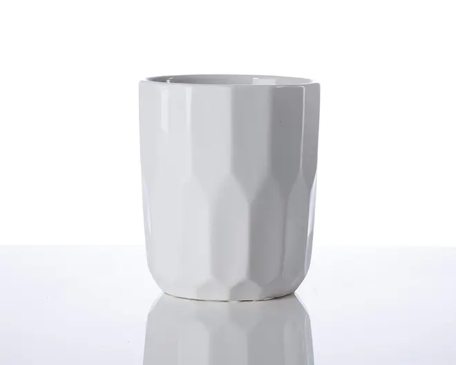 En hvid keramikkop med et moderne, facetslebet design. Overfladen har geometriske, kantede mønstre, der giver koppen et tekstureret udseende. Koppen har en glat kant og en blank finish, hvilket giver et stilrent og moderne udtryk.