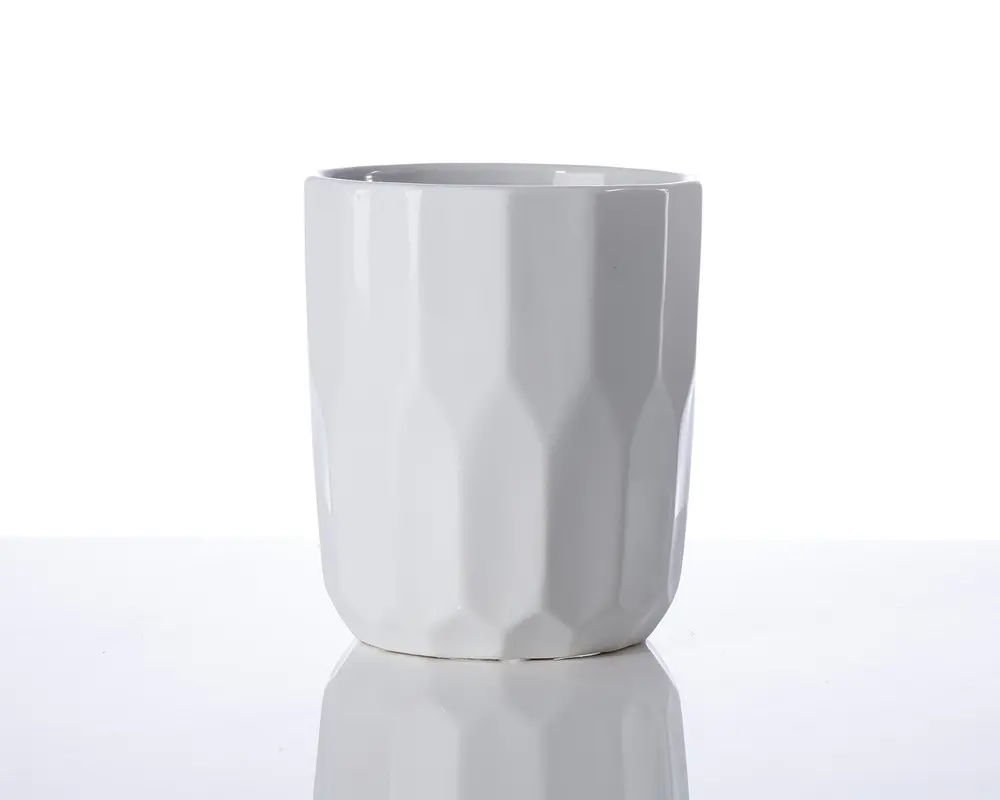 En hvid keramikkop med et moderne, facetslebet design. Overfladen har geometriske, kantede mønstre, der giver koppen et tekstureret udseende. Koppen har en glat kant og en blank finish, hvilket giver et stilrent og moderne udtryk.